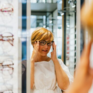 Adult woman trying on eyeglasses at an optical store, looking in a mirror.