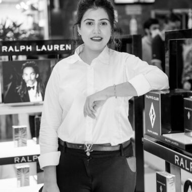 Black and white photo of a woman standing in a store next to perfume displays.