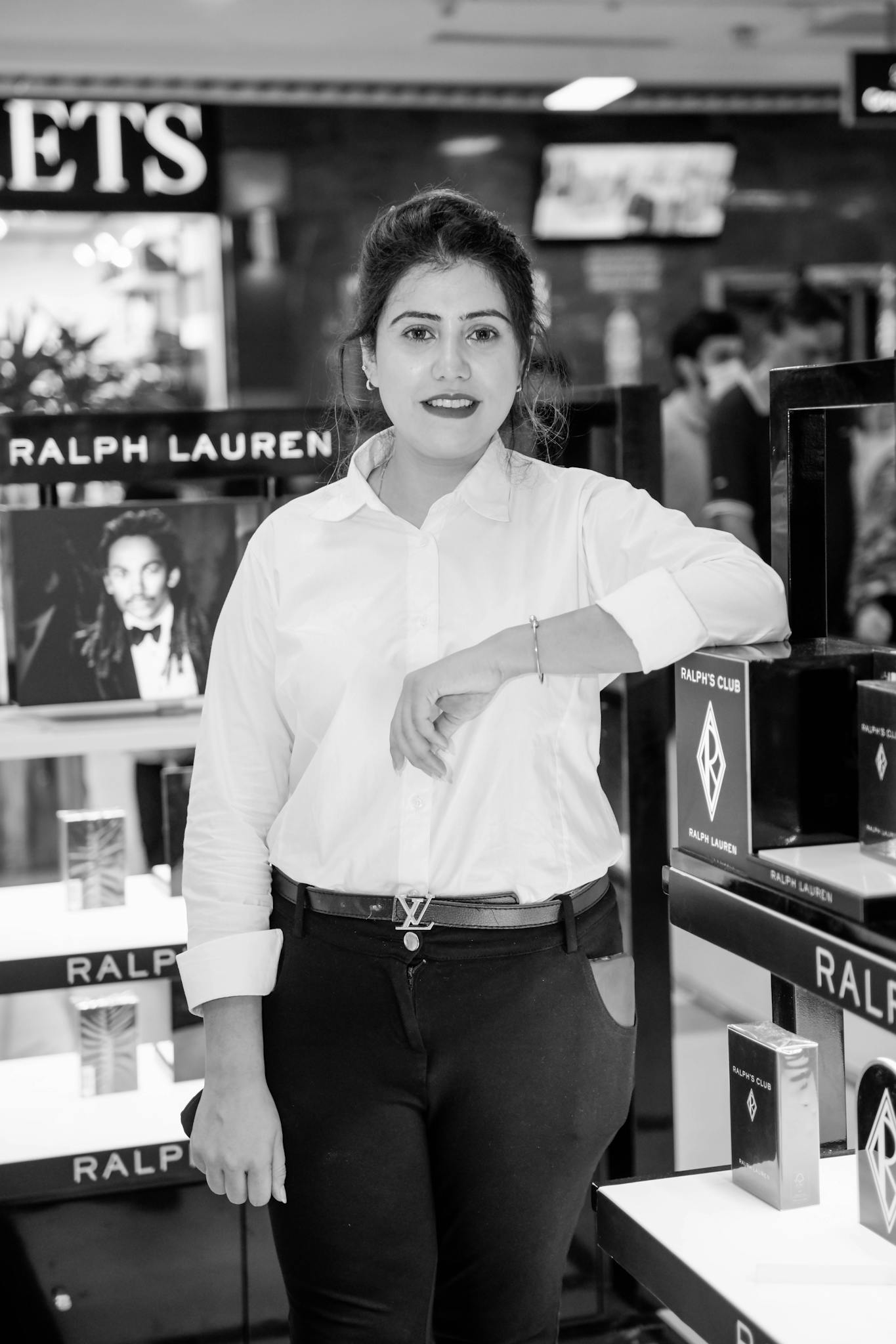 Black and white photo of a woman standing in a store next to perfume displays.